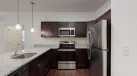 This single-floor residence offers a thoughtfully designed open-concept layout that seamlessly connects the living area to the kitchen, creating a spacious and inviting atmosphere throughout. Rich hardwood-style flooring runs consistently across the entire unit, lending warmth and cohesion to every room.

The kitchen is a standout feature, equipped with a full suite of stainless steel appliances including a French door refrigerator, electric range, and over-the-range microwave. Dark espresso cabinetry with brushed nickel hardware contrasts beautifully with the light granite countertops, while pendant lighting above the kitchen island adds a refined finishing touch.

The bedrooms are generously proportioned, each featuring ceiling fans and large windows that allow for ample natural light. The primary bedroom benefits from a walk-in closet, providing substantial storage. An additional bedroom includes a double-door closet for convenient organization.

Two bathrooms serve the residence. The primary bath features a standalone walk-in shower with sliding glass doors and a granite-topped vanity with dark cabinetry. The secondary bathroom offers a full soaking tub and shower combination, paired with a matching granite vanity. Both bathrooms continue the consistent design language found throughout the home, delivering a polished and cohesive aesthetic.