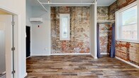 Located at 859 McCallie Ave in Chattanooga, TN, this efficiently designed single-floor unit offers a compelling mix of historic industrial character and contemporary updates. The main living area immediately draws attention with its striking exposed brick accent wall, which adds rich texture and warmth against the soft gray painted walls. Wood-look plank flooring runs throughout, providing a cohesive and durable foundation underfoot. Multiple windows invite generous natural light into the space, enhancing its open and airy feel despite its compact footprint.

The kitchen is well-appointed with white shaker-style cabinetry, white countertops, and a full suite of stainless steel appliances, including a refrigerator, gas range, dishwasher, and built-in microwave. A stainless steel sink and an in-unit washer round out the kitchen's practical offerings. Pendant lighting above adds a modern finishing touch.

The bathroom features a clean, all-white walk-in shower, a toilet, and a pedestal sink, complemented by built-in wire shelving for storage and neutral tile flooring. Exposed overhead piping in the living area reinforces the building's industrial heritage, while a wall-mounted mini-split HVAC unit ensures year-round comfort. This unit presents a distinctive urban living experience in the heart of Chattanooga.
