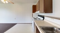 This compact one-bedroom, one-bathroom unit is located in Kenosha, Wisconsin, offering a practical and efficient layout across a single floor. The kitchen features warm wood-toned cabinetry lining the walls in an L-shaped configuration, providing ample upper and lower storage. Light-colored countertops offer generous prep space, and the room is finished with durable tile flooring. A stainless steel sink and electric range complete the functional setup.

The bedroom is a comfortable, carpeted space that benefits from a large sliding window overlooking a lush, green outdoor setting with mature trees — filling the room with natural light. A ceiling fan with a light fixture adds to the room's comfort, and a baseboard heating unit runs along the exterior wall. The overall feel is quiet and serene, with views that connect the interior to the surrounding landscape.

The bathroom is thoughtfully designed with accessibility in mind, featuring multiple stainless steel grab bars positioned near the bathtub and toilet, a handheld showerhead, and a pull-cord fixture. The mosaic tile flooring adds a classic touch to the well-maintained space.

A hallway connects the rooms, contributing to an efficient flow throughout the unit. The straightforward, functional design makes this an accessible and practical living space.