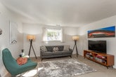 This single-floor residence offers a thoughtfully organized layout encompassing a living room, dining area, kitchen, multiple bedrooms, and two bathrooms. The living room provides a comfortable gathering space with carpet flooring, a large window that draws in natural light and outdoor views, and a textured ceiling. Adjacent to it, the dining area accommodates a round glass-top table beneath a bright window, complemented by tile flooring and a colorful art piece on the wall.

The kitchen features warm oak cabinetry with ample upper and lower storage, light countertops, a stainless steel sink, and a dishwasher, all set on easy-care tile flooring. The bedrooms are carpeted and include windows that invite natural light; one bedroom features a built-in closet, while another offers space for both sleeping and a dedicated workspace. Each room carries a clean, neutral palette.

The two bathrooms share a classic design with oak vanities, mirrored medicine cabinets, and tile flooring. One bathroom includes warm-toned wall tile halfway up, while the other maintains a clean white aesthetic. Together, the spaces offer a functional and cohesive living environment with a welcoming, homey ambiance throughout.
