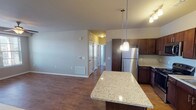 This single-floor residence offers a thoughtfully designed open-concept layout that seamlessly connects the kitchen and living areas. The kitchen serves as the heart of the home, showcasing rich dark-wood cabinetry, granite countertops, and a full suite of stainless steel appliances including a refrigerator, range, microwave, and dishwasher. A central island with a matching granite surface provides additional prep space and doubles as a casual dining area, illuminated by stylish pendant lighting. A wine rack built into the upper cabinetry adds a distinctive touch. Warm hardwood-style flooring runs throughout the main living and kitchen areas, while a ceiling fan anchors the spacious living room, enhancing both comfort and airflow. The bedrooms are finished with plush carpeting and feature large windows fitted with blinds, allowing for generous natural light and views of the surrounding neighborhood. Ceiling fans are present in the primary bedroom areas for added comfort. The bathrooms are clean and functional, each featuring a tub-shower combination with a curved curtain rod, hardwood-style flooring, and granite-topped vanities. The overall aesthetic is modern and practical, with neutral tones throughout creating a cohesive and inviting atmosphere.