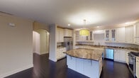This single-floor residence showcases a thoughtfully designed layout with refined finishes throughout. The gourmet kitchen is a standout feature, outfitted with cream-toned cabinetry, rich dark granite countertops, a decorative mosaic tile backsplash, stainless steel appliances, and a generously sized center island topped with matching granite. A bold geometric drum pendant light anchors the space, while dark hardwood flooring extends seamlessly into the adjacent open living area, which benefits from recessed lighting and crown molding details.

The bedrooms feature plush carpeting and warm neutral tones. The primary bedroom is distinguished by a tray ceiling with cove lighting and an elegant crystal chandelier, while a secondary bedroom offers natural light through multiple windows with outdoor views.

The primary bathroom is a luxurious retreat, showcasing dark emperador marble flooring and accent walls, dual vanities with white cabinetry and dark granite countertops, a freestanding clawfoot soaking tub, a glass-enclosed shower, and a crystal pendant light. A secondary bathroom continues the refined aesthetic with marble tile flooring, a tub-shower combination, and a dark granite-topped vanity with cream cabinetry.
