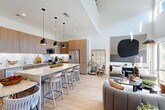 Located at 1 Riva Row in Spring, TX, this contemporary two-story home offers a thoughtfully designed layout spread across two floors. The main level centers around a striking open-concept living, dining, and kitchen area bathed in natural light from floor-to-ceiling windows. The kitchen is a standout, featuring warm wood cabinetry, a marble-style tile backsplash, stainless steel appliances, and a large waterfall-edge island with bar seating — all illuminated by sleek pendant lighting. Light hardwood flooring unifies the main living spaces, while soaring ceilings amplify the sense of openness. A well-appointed half bath on the main floor adds convenience for guests. Upstairs, two generously sized bedrooms each offer access to their own bathrooms. The primary suite includes a spa-inspired en-suite bathroom with a freestanding soaking tub, glass-enclosed walk-in shower, dual-sink vanity with wood cabinetry, and a spacious walk-in closet with built-in shelving. A versatile loft, dedicated office, and laundry room round out the upper level. With four closets total and a clean, modern aesthetic throughout, this home delivers both functional living and refined style.