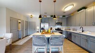 Located at 100 Oakview Dr in Trumbull, Connecticut, this single-floor residence offers a thoughtfully designed layout with modern finishes throughout. The kitchen is a standout feature, showcasing slate-gray shaker cabinetry extending to the ceiling, a white subway tile backsplash, stainless steel appliances including a gas range, microwave, refrigerator, and dishwasher, and a central island with seating illuminated by stylish pendant lights. Warm hardwood-style flooring flows throughout the main living areas. The living room is bright and welcoming, with large windows providing ample natural light and a neutral color palette accented by warm gold tones. The dining area features a textured accent wall, glass-top dining table, and access to an outdoor balcony. The primary bedroom offers a serene retreat with soft, neutral tones and decorative wall art, while the secondary bedroom includes generous dresser storage and natural window light. Two well-finished bathrooms serve the residence: the primary bath features a tiled walk-in shower and extended vanity with dual sinks, while the secondary bath includes a tiled tub-shower combo and gray vanity cabinetry. The cohesive design aesthetic, combining gray, cream, and gold accents, creates an elegant and contemporary ambiance throughout.