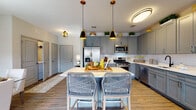 Located at 100 Oakview Dr in Trumbull, Connecticut, this single-floor residence offers a thoughtfully designed layout with modern finishes throughout. The kitchen is a standout feature, showcasing slate-gray shaker cabinetry extending to the ceiling, a white subway tile backsplash, stainless steel appliances including a gas range, microwave, refrigerator, and dishwasher, and a central island with seating illuminated by stylish pendant lights. Warm hardwood-style flooring flows throughout the main living areas. The living room is bright and welcoming, with large windows providing ample natural light and a neutral color palette accented by warm gold tones. The dining area features a textured accent wall, glass-top dining table, and access to an outdoor balcony. The primary bedroom offers a serene retreat with soft, neutral tones and decorative wall art, while the secondary bedroom includes generous dresser storage and natural window light. Two well-finished bathrooms serve the residence: the primary bath features a tiled walk-in shower and extended vanity with dual sinks, while the secondary bath includes a tiled tub-shower combo and gray vanity cabinetry. The cohesive design aesthetic, combining gray, cream, and gold accents, creates an elegant and contemporary ambiance throughout.