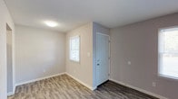 This single-story, 2-bedroom, 1-bathroom residence offers a well-organized layout designed for comfortable, everyday living. The main living area features durable wood-look plank flooring in a warm gray tone, neutral painted walls, and a window fitted with blinds that allows natural light to fill the space. A dedicated entryway with a paneled door provides a welcoming transition into the home.

The galley-style kitchen is efficiently designed with white cabinetry, granite-look countertops, a stainless steel sink, and black appliances including an electric range and dishwasher. An under-cabinet range hood completes the functional cooking space.

Both bedrooms are generously sized, with one featuring soft wall-to-wall carpeting and a window that brings in natural light, creating a comfortable and restful environment. The second bedroom also offers hardwood-style flooring and a window with blinds.

The bathroom is clean and straightforward, appointed with a full-size soaking tub and shower combination featuring chrome fixtures, a toilet, and a towel bar. The neutral color palette throughout the unit creates a cohesive and move-in-ready atmosphere.

A centrally located hallway connects the living spaces and provides access to the bedrooms and bathroom, keeping the floor plan easy to navigate. The overall design emphasizes clean lines, low-maintenance finishes, and practical functionality.