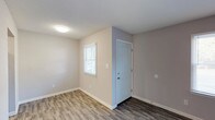 This single-story, 2-bedroom, 1-bathroom residence offers a well-organized layout designed for comfortable, everyday living. The main living area features durable wood-look plank flooring in a warm gray tone, neutral painted walls, and a window fitted with blinds that allows natural light to fill the space. A dedicated entryway with a paneled door provides a welcoming transition into the home.

The galley-style kitchen is efficiently designed with white cabinetry, granite-look countertops, a stainless steel sink, and black appliances including an electric range and dishwasher. An under-cabinet range hood completes the functional cooking space.

Both bedrooms are generously sized, with one featuring soft wall-to-wall carpeting and a window that brings in natural light, creating a comfortable and restful environment. The second bedroom also offers hardwood-style flooring and a window with blinds.

The bathroom is clean and straightforward, appointed with a full-size soaking tub and shower combination featuring chrome fixtures, a toilet, and a towel bar. The neutral color palette throughout the unit creates a cohesive and move-in-ready atmosphere.

A centrally located hallway connects the living spaces and provides access to the bedrooms and bathroom, keeping the floor plan easy to navigate. The overall design emphasizes clean lines, low-maintenance finishes, and practical functionality.