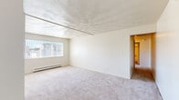 Located at 1219 E Bellows St in Mount Pleasant, Michigan, this single-floor unit offers a practical and well-organized layout. The spacious living area is finished with neutral-toned carpet and features a textured ceiling, a track lighting fixture, and a large window with vertical blinds that allows natural light to fill the room. Baseboard heating units are present throughout the space, ensuring consistent warmth. The galley-style kitchen is equipped with white appliances including a refrigerator, electric range, and dishwasher, complemented by warm wood-toned cabinetry, butcher block-style countertops, a double basin sink, and durable tile flooring. A doorway from the kitchen leads to an adjacent dining or utility area, also finished with matching tile. The bedrooms are carpeted and feature warm wood-toned bi-fold closet doors offering built-in storage with shelving and hanging rods. Each bedroom includes a window with blinds providing natural light and views of the surrounding neighborhood. The overall color palette throughout the unit is light and neutral, contributing to a clean and functional ambiance well-suited for everyday living.