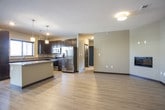 This single-floor residence presents a thoughtfully designed open-concept layout that seamlessly connects the kitchen, dining, and living areas. The living space features light hardwood-style flooring, neutral taupe walls, dark baseboards, and a sleek built-in fireplace, creating a contemporary and cohesive aesthetic throughout.

The kitchen is a standout feature, equipped with rich dark espresso cabinetry extending to the ceiling, granite countertops, and a full suite of stainless steel appliances including a refrigerator with ice dispenser, electric range, and over-the-range microwave. A central island with matching granite provides additional workspace and is illuminated by pendant lighting above.

The bedrooms are carpeted for comfort, each featuring neutral tones, dark door trim, and windows that allow natural light. The primary bathroom includes a double-sink vanity topped with granite countertops, dark cabinetry, and a large mirror, while an additional bathroom features a full tub-shower combination with chrome fixtures and coordinating finishes throughout. The overall design maintains a modern, consistent palette of warm neutrals and dark accents.