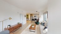 Located at 360 Huguenot Street in New Rochelle, NY, this single-floor residence offers a thoughtfully designed open-concept layout that seamlessly connects the living, dining, and kitchen areas. Light hardwood flooring flows throughout the main living space, complementing the clean white walls and creating a bright, airy atmosphere. Large windows frame views of the surrounding New Rochelle cityscape, filling the space with abundant natural light.

The kitchen is outfitted with modern two-tone cabinetry in gray and warm wood tones, white quartz countertops, and a full suite of stainless steel appliances, including a gas range, microwave, dishwasher, and refrigerator. Recessed lighting and a window over the sink add both functionality and brightness.

The living area is generously proportioned, accommodating a full seating arrangement alongside a dedicated dining space. The bedroom features dual windows with city views, a walk-in closet, and light wood flooring, offering a calm and comfortable retreat.

The bathroom is finished with large-format tile throughout, a white vanity with dark countertop, and a shower-tub combination, delivering a clean and polished aesthetic consistent with the rest of the residence.