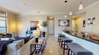 Located at 1951 Hunter Rd in San Marcos, TX, this well-appointed 2-bedroom, 2-bathroom residence offers a thoughtfully designed single-floor layout with a welcoming entrance and a hallway that connects all living areas. The open-concept great room seamlessly unites the living, dining, and kitchen spaces, all finished with polished stained concrete floors and crown molding throughout. Large windows flood the living area with natural light, while a sliding glass door in the dining area opens directly onto a private balcony with outdoor views. The kitchen is anchored by a dark-granite peninsula with bar stool seating, rich dark-wood cabinetry, stainless steel appliances, a pantry, and pendant lighting with additional track lighting overhead. Both bedrooms are generously sized, featuring neutral tones, crown molding, and ample closet space — five closets in total across the home. The bathrooms are finished with tiled tub-shower surrounds, dark wood vanities, and white countertops. A dedicated in-unit laundry area with built-in shelving adds everyday convenience. The layout also includes a hallway connecting the bedrooms, providing a clear separation between the living and private areas of the home.
