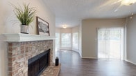 Located at 5401 Burnham Dr in Corpus Christi, TX, this single-story residence offers a thoughtfully designed layout with a warm, neutral color palette throughout. The living area serves as the heart of the home, anchored by a striking brick fireplace with a white mantle that adds classic charm. Durable hardwood-style flooring runs throughout the main living spaces, complemented by vaulted ceilings with ceiling fans that enhance the sense of openness and airflow. A bay-style window grouping floods the living area with natural light, while a sliding glass door provides direct access to an outdoor area. The kitchen is appointed with rich, dark cabinetry, light countertops, and modern stainless steel appliances including a refrigerator and range, offering a functional and stylish workspace. The bedroom features plush carpeting, dual windows for ample natural light, vaulted ceilings with a ceiling fan, and mirrored sliding closet doors that add depth to the room. The bathroom is well-appointed with dark wood cabinetry, a large vanity mirror, globe lighting, and overhead storage cabinets for added convenience. The textured ceilings throughout add a layer of detail to the overall design of this comfortable Corpus Christi residence.