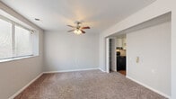 This single-floor, 2-bedroom, 1-bathroom unit offers a straightforward and functional layout designed for comfortable everyday living. The living area is finished with neutral-toned carpet and features a ceiling fan with integrated lighting, providing both comfort and airflow. A wide open passageway connects the living space directly to the kitchen, which is equipped with black appliances including an electric range, white upper cabinetry, and an adjacent built-in shelving nook — offering convenient storage and a practical workspace.

The primary bedroom is generously sized, offering ample room for furnishings, and is brightened by two windows fitted with horizontal blinds that allow for adjustable natural light. The second bedroom is more compact but equally well-lit, featuring its own window with blinds and soft carpeting underfoot, making it suitable as a guest room, home office, or additional sleeping space.

A connecting hallway links the bedrooms to the full bathroom, which includes a tub-shower combination with white subway tile surround and brushed nickel fixtures, as well as hardwood-style flooring. Throughout the unit, neutral gray walls, clean white trim, and consistent carpeting create a cohesive, move-in-ready aesthetic.