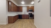This single-floor unit offers a thoughtfully designed layout that balances functionality and comfort throughout. The kitchen is a standout feature, boasting rich warm-toned cabinetry, light-colored countertops, and a full suite of stainless steel appliances including a range, over-the-range microwave, refrigerator, and black dishwasher. Light wood-style flooring runs throughout the kitchen and into the connecting hallway and living areas, lending a clean, cohesive aesthetic. A set of double panel doors provides convenient closet storage near the entryway, adding practical utility to the open layout. The living area is bright and open, benefiting from natural light via a glass door and ceiling fan overhead. Wood-style flooring continues here, creating a warm, inviting atmosphere. The bedroom is finished with plush carpet and features a closet rod and natural light from a window with blinds, offering a quiet and comfortable retreat. The bathroom is well-appointed with a double-sink vanity topped with a light countertop, rich wood cabinetry, large mirror, and tile flooring. A separate water closet area houses the toilet and a full tub and shower combination with built-in shelving, completing the functional design of this unit.