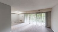 Located at 5518 Tomahawk Dr in Greensboro, North Carolina, this single-floor residence offers a well-organized layout designed for comfortable everyday living. The spacious living room is a standout feature, highlighted by a wall of floor-to-ceiling sliding glass doors dressed with vertical blinds that flood the room with natural light and provide lush, tree-lined outdoor views. Soft carpeting and a textured ceiling lend warmth and a classic feel to this welcoming common area. The kitchen has been tastefully updated with crisp white shaker-style cabinetry, black hardware, granite-look countertops, a subway tile backsplash, and a stainless steel sink. Black appliances, including a refrigerator and range, provide a sharp contrast to the bright cabinetry, while a dedicated walk-in pantry offers generous storage. Wood-look plank flooring grounds the kitchen and adjoining spaces. The bedrooms are carpeted and bathed in natural light from well-placed windows overlooking greenery, each equipped with a ceiling fan for year-round comfort. Closet access is conveniently integrated into the bedroom layouts. The bathroom features wood-look tile flooring and clean white finishes throughout. Neutral gray tones used consistently across the home create a cohesive, move-in-ready aesthetic.