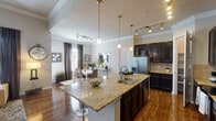 This two-story home in Conroe, TX offers a thoughtfully designed layout across four bedrooms and three bathrooms. The main floor showcases a seamless open-concept living area where the living room, dining space, and kitchen flow together naturally. Rich hardwood flooring runs throughout, complemented by crown molding and ceiling fans that add a polished finish.

The kitchen is a standout feature, equipped with dark espresso cabinetry, granite countertops, stainless steel appliances, a tile backsplash, and a large center island with bar seating and pendant lighting overhead. Track lighting and pendant fixtures illuminate the space, while a dedicated pantry provides ample storage.

The living and dining areas benefit from abundant natural light through multiple windows dressed with blinds and drapes. Vaulted ceiling details in the living room lend an airy, open quality to the space.

The bedrooms are carpeted and well-proportioned, with crown molding and generous natural light. One bedroom features a charming built-in window seat. The bathrooms include full tub-and-shower combinations with elegant stone-look tile surrounds. The home's two-story layout provides functional separation between living and private spaces.