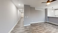 Located at 1230 Elm St in Manchester, NH, this well-appointed two-bedroom, one-bathroom unit offers a thoughtfully designed single-floor layout with contemporary finishes throughout. The combined kitchen and living area serves as the heart of the home, showcasing a sleek peninsula with a light stone countertop, crisp white shaker cabinetry, a white subway tile backsplash, and a full suite of stainless steel appliances including a range, built-in microwave, and French door refrigerator. Pendant lighting above the peninsula adds a refined touch, while large floor-to-ceiling windows flood the space with natural light and frame views of surrounding greenery. Wood-style plank flooring runs throughout the main living areas, complementing the neutral gray palette. The hallways are bright and open, connecting the living space to the private quarters. The generously sized primary bedroom features corner windows that invite natural light, while the second bedroom offers similar understated comfort. Both bedrooms are carpeted and include access to a dedicated walk-in closet with wire shelving. The full bathroom is finished with a marble-top vanity, wood-style flooring, and a tub-shower combination with matte black fixtures. Clean lines, modern hardware, and a cohesive neutral color scheme give the entire unit a polished, move-in-ready feel.
