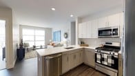 Located at 665–711 Commerce Dr in Fairfield, Connecticut, this one-bedroom, one-bathroom residence with a den offers a thoughtfully designed single-floor layout ideal for modern living. The open-concept floor plan seamlessly connects the kitchen and living area, creating a bright and cohesive space. The kitchen is outfitted with stainless steel appliances, including a gas range, built-in microwave, and dishwasher. Sleek, two-tone cabinetry — white uppers paired with warm wood-toned lower cabinets — frames a generous quartz countertop with a peninsula island that provides additional prep space and casual seating. A subway tile backsplash and recessed lighting add polished finishing touches. Dark hardwood-style flooring anchors the kitchen and flows throughout the main living areas, providing a striking contrast to the light, neutral color palette. The living area benefits from large windows that invite an abundance of natural light, enhancing the open and airy ambiance of the space. The additional den offers flexible space that can serve as a home office, reading nook, or guest room. Overall, the residence combines contemporary design with functional living, making it a well-appointed home in Fairfield, CT.