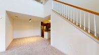 Located at The Reserve At The Boulevard in Yaphank, New York, this two-story residence offers a thoughtfully designed layout with impressive architectural details throughout. The main living area immediately captures attention with its soaring double-height ceilings and an abundance of natural light streaming through large windows and a sliding glass door, which opens to an outdoor balcony. A classic wood-railed staircase with white balusters serves as a central architectural feature, connecting both floors with elegance.

The kitchen is well-appointed with dark espresso cabinetry, granite countertops, a decorative tile backsplash, and a full suite of stainless steel appliances including a gas range, microwave, and refrigerator. A louvered door leads conveniently to an adjacent utility area. The main level also includes a closet and a full bathroom featuring wood-look flooring, a granite-topped vanity, and a soaking tub with shower.

Upstairs, the spacious second level continues the open, airy feel with high ceilings and plush carpeting. A generously sized walk-in closet with wire shelving on multiple walls provides excellent storage. A second full bathroom mirrors the finishes of the first, with a granite vanity, dark cabinetry, and a tub-shower combination. Throughout, neutral tones and quality finishes create a clean, comfortable living environment.