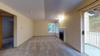 This single-floor residence offers a well-organized layout with a variety of comfortable living spaces. The living room is a standout area, featuring vaulted ceilings that lend a sense of openness and height, along with a classic fireplace framed by a white mantel. Natural light filters in through a window overlooking lush greenery, while track lighting and a baseboard heating unit add to the room's functionality. Plush carpet flows throughout the living and bedroom areas.

The kitchen is efficiently designed with an L-shaped layout, white cabinetry trimmed in warm wood tones, laminate countertops, a double sink, a dishwasher, and an electric range. A skylight and window above the sink bring in ample natural light, and durable wood-look vinyl flooring completes the space.

The unit includes multiple bedrooms, each carpeted and finished with neutral warm tones. One bedroom features vaulted ceilings and a window with green views, while another includes a sliding wood-panel closet door. Additional rooms provide flexible use as bedrooms or office space.

Two full bathrooms each include a tub-shower combination, toilet, vanity with generous mirror, and tiled accents. The overall aesthetic is clean, neutral, and move-in ready.