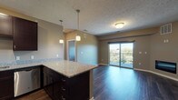This single-floor residence offers a thoughtfully designed open layout that connects the kitchen, dining, and living areas seamlessly. The kitchen is well-equipped with rich dark espresso cabinetry extending to the ceiling, granite countertops, a full suite of stainless steel appliances including a refrigerator with ice maker, range, microwave, and dishwasher, complemented by pendant lighting over the granite-topped island. Dark hardwood-style flooring flows throughout the main living areas, anchoring the neutral warm-toned walls.

The spacious living area is highlighted by a built-in electric fireplace and direct access to a private balcony through a sliding glass door, offering outdoor views of surrounding greenery. The entry features a paneled front door alongside a closet for additional storage.

Two generously sized bedrooms are finished with plush carpeting and windows that bring in natural light and exterior views. The unit includes two bathrooms, each featuring granite-topped dark vanities and undermount sinks. One bathroom offers a tub-shower combination, while the second provides a dedicated walk-in shower, both finished with hardwood-style flooring consistent with the home's overall aesthetic.