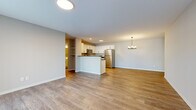 This well-appointed single-floor unit offers a thoughtfully designed layout that maximizes functionality and comfort. The open-concept kitchen and living area serves as the heart of the home, featuring warm wood-look luxury vinyl plank flooring that flows seamlessly throughout the space. The kitchen is outfitted with crisp white shaker-style cabinetry, dark countertops, a full suite of stainless steel appliances including a refrigerator, range, over-the-range microwave, and dishwasher, and a peninsula that provides additional prep space and casual seating. A pendant chandelier anchors the dining area, adding a refined touch to the open layout. The living area is generously sized, offering ample room for a variety of furniture arrangements, with a front entry door and sliding door access that bring in natural light. Two bathrooms serve the unit: one features a walk-in shower with a full white surround, while the second includes a full vanity with white cabinetry and a tub-shower combination. A dedicated utility room provides practical storage and mechanical access. The attached garage offers a spacious concrete-floored area with an automatic opener and paneled garage door with transom windows, providing secure and convenient parking or additional storage.