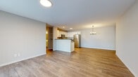This well-appointed single-floor unit offers a thoughtfully designed layout that maximizes functionality and comfort. The open-concept kitchen and living area serves as the heart of the home, featuring warm wood-look luxury vinyl plank flooring that flows seamlessly throughout the space. The kitchen is outfitted with crisp white shaker-style cabinetry, dark countertops, a full suite of stainless steel appliances including a refrigerator, range, over-the-range microwave, and dishwasher, and a peninsula that provides additional prep space and casual seating. A pendant chandelier anchors the dining area, adding a refined touch to the open layout. The living area is generously sized, offering ample room for a variety of furniture arrangements, with a front entry door and sliding door access that bring in natural light. Two bathrooms serve the unit: one features a walk-in shower with a full white surround, while the second includes a full vanity with white cabinetry and a tub-shower combination. A dedicated utility room provides practical storage and mechanical access. The attached garage offers a spacious concrete-floored area with an automatic opener and paneled garage door with transom windows, providing secure and convenient parking or additional storage.