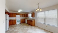 This three-story home offers a functional and straightforward layout designed for comfortable everyday living. The kitchen is a standout feature, presenting an L-shaped or U-shaped configuration with warm honey-toned wood cabinetry, light laminate countertops, and tile flooring in a classic checkered pattern. White appliances—including a range, over-the-range microwave, refrigerator, and dishwasher—are included. A chandelier and multiple windows allow natural light to brighten the space. The dedicated laundry area houses a full-size washer and dryer set beneath wire shelving for added storage convenience. Bedrooms are carpeted in a neutral beige tone and include ceiling fans with integrated lighting. Windows fitted with horizontal blinds bring in natural light while maintaining privacy. The bathrooms feature tile flooring and wood vanities with light countertops. One bathroom includes a walk-in shower with a glass-framed enclosure, while another offers a shower-tub combo. Stairways connect the three levels, with carpeted landings maintaining a cohesive look throughout. The overall aesthetic is clean, neutral, and move-in ready.