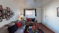 Located at 1207 N 48th St in Phoenix, Arizona, this single-story residence offers a well-organized layout across multiple rooms designed for comfortable everyday living. The living room serves as a welcoming central gathering space, featuring rich dark hardwood-style flooring, a large window dressed with vertical blinds and draped curtains that invite natural light, and ample room for seating. Wall art adds a decorative focal point to the space. The kitchen is efficiently laid out with warm cherry-toned cabinetry, dark granite-style countertops, black appliances including a range and refrigerator, and the same wood-style flooring that carries throughout the common areas. Multiple bedrooms provide comfortable accommodations, each carpeted for warmth and featuring windows with decorative curtain treatments. The primary bedroom is notably spacious, with a textured ceiling, direct access to a closet area, and room for substantial furniture. Additional bedrooms offer similarly cozy environments with natural light. The bathroom is well-appointed with dark wood vanity cabinetry, granite-style countertops, a framed mirror, and hardwood-style flooring. Throughout the home, textured ceilings and neutral wall tones create a consistent and cohesive aesthetic.