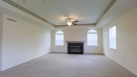 This two-story home offers a thoughtfully designed layout that balances comfort and elegance across two floors. The main living area immediately draws attention with its distinctive tray ceiling, which adds architectural depth and a sense of grandeur to the room. A ceiling fan is centrally mounted within the tray, providing both style and practical airflow throughout the space.

Two arched windows flank a classic fireplace, serving as the focal point of the living room. The arched design of the windows introduces a refined architectural touch while allowing generous amounts of natural light to illuminate the neutral-toned walls and plush wall-to-wall carpeting below. The fireplace features a clean, dark surround and mantel, offering a warm and inviting atmosphere.

The overall color palette is light and airy, with soft beige walls and matching carpet that create a calm, neutral canvas suitable for a variety of interior styles. Crown molding along the upper edges of the tray ceiling adds a finishing detail that enhances the room's polished appearance.

The two-floor layout provides ample separation between living and private spaces, making the home well-suited for both everyday living and entertaining. The combination of architectural details, natural light, and classic design elements gives this home a welcoming and timeless character throughout.