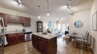 Located in Navarre, FL, this well-appointed 2-bedroom, 2-bathroom residence offers a thoughtfully designed single-level floor plan. The open-concept kitchen and living area serves as the heart of the home, where rich dark-wood cabinetry, granite countertops, and a central island with bar seating combine with a full suite of stainless steel appliances — including a refrigerator, range, microwave, and dishwasher — to create a highly functional cooking space. Warm wood-look flooring flows throughout the main living areas, complementing the bright, neutral color palette. The living room is bathed in natural light from French doors that open to a private outdoor area, and a ceiling fan adds comfort overhead. The primary bedroom features plush carpeting and direct access to a well-sized closet, while the second bedroom also offers carpeted flooring and a generous window. Both bathrooms are finished with dark-wood vanities, granite countertops, and tile-surround tub/shower combinations. The dual-sink primary bathroom adds an extra layer of convenience. Track lighting and pendant fixtures throughout enhance the overall ambiance, giving the space a clean, coastal-inspired character well-suited to the Florida Gulf Coast setting.