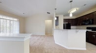 This single-story residence offers a thoughtfully designed open-concept layout that seamlessly connects the main living areas. The kitchen is a standout feature, equipped with rich dark espresso cabinetry reaching toward the ceiling, granite countertops, black appliances including a refrigerator, dishwasher, range, and microwave, and light tile flooring. A curved breakfast bar with pendant lighting above separates the kitchen from the adjoining living and dining areas, which are finished with neutral-toned carpet and warmed by a vaulted ceiling in the dining space. A chandelier and large window flood the dining area with natural light.

The bedrooms are generously sized, each featuring plush carpet, neutral walls, and windows with blinds that allow ample natural light. One bedroom includes a spacious walk-in closet outfitted with wire shelving and hanging rods for versatile storage. The bathroom is finished with large-format tile flooring, a dark-cabinet vanity with a white countertop, a framed mirror, and a shower-tub combination. A dedicated laundry area accommodates a full-sized washer and includes shelving overhead, adding functional convenience to the layout.