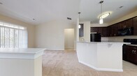 This single-story residence offers a thoughtfully designed open-concept layout that seamlessly connects the main living areas. The kitchen is a standout feature, equipped with rich dark espresso cabinetry reaching toward the ceiling, granite countertops, black appliances including a refrigerator, dishwasher, range, and microwave, and light tile flooring. A curved breakfast bar with pendant lighting above separates the kitchen from the adjoining living and dining areas, which are finished with neutral-toned carpet and warmed by a vaulted ceiling in the dining space. A chandelier and large window flood the dining area with natural light.

The bedrooms are generously sized, each featuring plush carpet, neutral walls, and windows with blinds that allow ample natural light. One bedroom includes a spacious walk-in closet outfitted with wire shelving and hanging rods for versatile storage. The bathroom is finished with large-format tile flooring, a dark-cabinet vanity with a white countertop, a framed mirror, and a shower-tub combination. A dedicated laundry area accommodates a full-sized washer and includes shelving overhead, adding functional convenience to the layout.