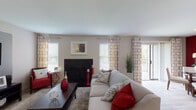 This single-floor residence in Lexington, Kentucky offers a cohesive and stylish interior defined by a bold red and neutral color palette carried consistently throughout the space. The living room serves as the heart of the home, featuring wood-look flooring, a fireplace with a sleek black surround, a dedicated media wall with a built-in accent niche, and multiple windows dressed with patterned curtains that allow ample natural light. Sliding glass doors open directly to a private balcony, extending the living space outdoors. The adjacent dining area features a striking red accent wall, a glass-top dining table, and its own access to the balcony, creating a bright and inviting atmosphere. The kitchen is equipped with dark cabinetry, granite countertops, stainless steel appliances including a refrigerator and microwave, and a skylight overhead that floods the space with natural light. A peninsula with a sink adds functional counter space. The bedrooms offer comfortable retreats, each with plush carpeting, generous window coverage, and coordinated accent walls. Two bathrooms are finished with granite-top dark vanities and wood-look tile flooring — one featuring a soaking tub and the other a walk-in shower.