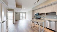 Located at 880 Pacific St in Stamford, Connecticut, this contemporary one-bedroom, one-bathroom residence offers a thoughtfully designed open-concept layout finished with light hardwood-style flooring throughout. The combined kitchen and living area serves as the heart of the home, featuring a sleek, modern kitchen outfitted with light wood cabinetry extending to the ceiling, a subway tile backsplash, stainless steel appliances including a gas range, built-in microwave, and French door refrigerator, and a freestanding island with a quartz-style countertop ideal for casual dining or meal prep. Track lighting accents the kitchen, while large sliding glass doors flood the living area with natural light and provide access to a private balcony. The spacious bedroom is a serene retreat, highlighted by dramatic floor-to-ceiling windows that frame breathtaking views of a marina and waterway. Two closets provide generous storage. The full bathroom features a modern floating vanity with an undermount sink, a backlit mirror, quartz countertop, and tiled shower. An in-unit laundry area adds everyday convenience. Neutral tones and clean lines throughout create a bright, contemporary ambiance.