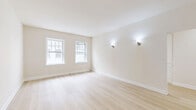 Located at 702 S Mariposa Ave in the heart of Los Angeles' Koreatown neighborhood, this two-bedroom, one-bathroom unit offers a thoughtfully laid-out single-floor plan with a clean, modern aesthetic. Light-toned hardwood flooring runs throughout, complementing the warm neutral walls and white trim that give the space a bright, cohesive feel.

The living and dining areas provide comfortable gathering spaces, while two connecting hallways ensure easy flow between rooms. The kitchen is a standout feature, showcasing beadboard-style grey cabinetry, white countertops, a matte black faucet with an undermount stainless steel sink, and herringbone-pattern tile flooring — all bathed in natural light from an adjacent window.

Both bedrooms are well-proportioned, with the primary bedroom offering generous space. Each room features large, multi-pane windows that invite abundant natural light and offer views of the surrounding Los Angeles cityscape and neighborhood. Elegant wall sconces provide warm accent lighting throughout.

The bathroom impresses with floor-to-ceiling marble-effect tile in the walk-in shower, fitted with a sleek glass door and a dark bronze grab bar, adding a refined, upscale touch. The overall design is clean, minimal, and move-in ready, making this a well-appointed urban residence.