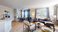 This single-floor residence offers a thoughtfully designed open-concept layout that seamlessly connects the living, dining, and kitchen areas. The living room is generously proportioned, featuring light hardwood flooring, crown molding, and multiple large windows dressed with plantation shutters and floor-length curtains that flood the space with natural light and offer views of lush greenery outside. An elegant arched architectural detail frames the transition between spaces, adding a refined touch to the interior design.

The dining area is positioned near a bay window arrangement, creating a bright and inviting atmosphere for meals. The kitchen is outfitted with white cabinetry, light stone countertops, stainless steel appliances including a range, built-in microwave, and dishwasher, and features a peninsula that provides additional prep space and casual seating potential.

Both bedrooms are carpeted for comfort, each receiving natural light through sizable windows with shutters. The rooms offer ample wall space for furnishings and décor. The bathroom is finished with wood-look flooring, a white vanity with an extended countertop, a full tub-shower combination with white tile surround, and a large mirror. Ceiling fans are present throughout, contributing to the home's functional and comfortable living environment.