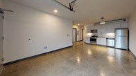 This contemporary single-floor live-work unit blends industrial character with modern finishes throughout. Polished concrete floors extend across the entire space, reflecting light and lending a sleek, urban aesthetic. The open main area is expansive and versatile, anchored by a glass-panel garage door that floods the space with natural light and offers views of the surrounding streetscape. An exposed metal duct adds to the industrial loft-style ambiance.

The kitchen is well-appointed with white cabinetry, light countertops, a classic subway tile backsplash, and a full suite of stainless steel appliances including an electric range, over-the-range microwave, dishwasher, and refrigerator. A pendant light fixture with an industrial flair hangs above, complementing the overall design.

Additional rooms include private spaces accessible from the main area, one of which features a wall-unit HVAC system and a window with outdoor views. The bathroom is finished with large-format gray tile surrounding a soaking tub and shower combination, paired with chrome fixtures. A dedicated laundry closet equipped with wire shelving and a washer hookup provides added functionality. Recessed lighting throughout keeps the space bright and well-illuminated.