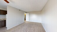 Located at 3528 E Second St in Tucson, AZ, this one-bedroom, two-bathroom unit offers a compact and efficient single-floor layout designed to maximize functionality. The living room provides a welcoming common area featuring plush wall-to-wall carpeting, neutral gray walls, a textured ceiling, and a ceiling fan with integrated lighting. A sliding glass door floods the space with natural light and offers outdoor access. Adjacent to the living room, the kitchen is equipped with dark wood cabinetry, a sink, and countertop space, providing a practical cooking area that flows seamlessly into the main living space. The bedroom is a comfortable retreat with soft carpeting, a window overlooking greenery, and direct access to one of the two bathrooms, which features dark wood vanity cabinetry and a well-lit mirror. A dedicated hallway connects the bedroom to a walk-in closet complete with built-in shelving, offering generous storage. The hallway also includes additional built-in cabinetry with a light countertop surface and wood-toned lower cabinets, adding practical storage and workspace. Light wood-style flooring in the hallway contrasts nicely with the carpeted living and sleeping areas, contributing to a layered, cohesive interior palette throughout this well-organized Tucson residence.