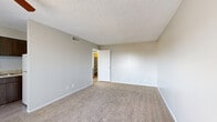 Located at 3528 E Second St in Tucson, AZ, this one-bedroom, two-bathroom unit offers a compact and efficient single-floor layout designed to maximize functionality. The living room provides a welcoming common area featuring plush wall-to-wall carpeting, neutral gray walls, a textured ceiling, and a ceiling fan with integrated lighting. A sliding glass door floods the space with natural light and offers outdoor access. Adjacent to the living room, the kitchen is equipped with dark wood cabinetry, a sink, and countertop space, providing a practical cooking area that flows seamlessly into the main living space. The bedroom is a comfortable retreat with soft carpeting, a window overlooking greenery, and direct access to one of the two bathrooms, which features dark wood vanity cabinetry and a well-lit mirror. A dedicated hallway connects the bedroom to a walk-in closet complete with built-in shelving, offering generous storage. The hallway also includes additional built-in cabinetry with a light countertop surface and wood-toned lower cabinets, adding practical storage and workspace. Light wood-style flooring in the hallway contrasts nicely with the carpeted living and sleeping areas, contributing to a layered, cohesive interior palette throughout this well-organized Tucson residence.