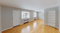 This single-floor space offers a clean, functional layout with consistent warm-toned hardwood flooring running throughout. The open living area is a highlight, featuring two windows fitted with blinds that allow ample natural light to fill the room, along with baseboard heating units positioned beneath each window. A front entry door opens directly into this spacious living area, which also includes a ceiling-mounted light fixture and access to adjoining rooms.

A dedicated bedroom provides a comfortable retreat, complete with its own window, baseboard heater, and a ceiling fan with an integrated light fixture, contributing to year-round comfort. The room's neutral gray walls and hardwood floors create a calm, versatile atmosphere.

The bathroom showcases classic design elements, including white subway tile walls accented with a black border, a black-and-white hexagonal mosaic tile floor, and a soaking tub. A window provides natural ventilation, while a granite-topped vanity adds a refined touch alongside gold-toned hardware throughout.

The kitchen, visible in the floor plan, is centrally positioned and features white cabinetry and essential appliances. Doorways with gold hardware connect the various spaces, maintaining a cohesive aesthetic. Overall, the unit presents a bright, well-appointed living environment.