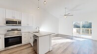 Located at 51 Hillside Rd in Pine Plains, NY, this two-floor home showcases a clean, modern design with consistent finishes throughout. The open-concept kitchen is a standout feature, equipped with white shaker cabinetry, stainless steel appliances, granite countertops, a peninsula with a built-in sink, and stylish pendant lighting. Soaring vaulted ceilings amplify the sense of space in the main living area, which is enhanced by a ceiling fan and a sliding glass door leading to an outdoor deck with views of the surrounding natural landscape. Wide-plank hardwood-style flooring runs throughout the main living spaces, lending warmth and continuity to the home's bright, airy aesthetic. A hallway with high ceilings and a decorative pendant light connects multiple rooms, including closets with wire shelving systems. The bathroom features marble-style tile flooring, a granite-topped white vanity, and clean, minimalist finishes. Bedrooms benefit from vaulted ceilings, ceiling fans, and abundant natural light through well-placed windows. The attached garage offers ample space with a concrete floor and an automatic opener, while the unfinished basement provides significant potential for future customization or additional storage.