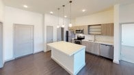 This single-floor residence offers a thoughtfully designed layout with contemporary finishes throughout. The kitchen serves as a central highlight, featuring stainless steel appliances including a refrigerator, range, microwave, and dishwasher, complemented by light wood cabinetry, open shelving, a subway tile backsplash, quartz countertops, a double-basin undermount sink, and a spacious central island with pendant lighting overhead. Dark hardwood-style flooring runs through the main living and kitchen areas, lending a warm, cohesive aesthetic.

The living area is open and bright, with clean white walls, elevated ceilings, and ample room for flexible furniture arrangements. The bedrooms are carpeted for comfort and each include a ceiling fan with a window fitted with horizontal blinds, allowing for natural light and ventilation control. A walk-in closet equipped with a full wire shelving and basket system provides generous, organized storage.

The bathrooms are finished with subway tile tub-surround enclosures, soaking tubs, dark hardwood-style flooring, and modern vanities with clean white countertops. A dedicated in-unit laundry room houses a full-size washer and dryer alongside a water heater, offering added convenience. Overall, the space presents a clean, modern aesthetic with practical, well-considered features throughout.