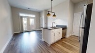 This contemporary apartment showcases a well-designed layout optimized for modern living. The heart of the home is an open-concept kitchen featuring crisp white cabinetry, stainless steel appliances, and a practical island with a built-in sink. Track lighting and pendant fixtures provide focused illumination. The kitchen flows seamlessly into living areas adorned with warm wood-look flooring.

A standout feature is the barn-style sliding door, adding rustic charm to the otherwise sleek design. The bathroom boasts a marble-look tiled shower, modern vanity, and continues the wood-look flooring. In-unit laundry facilities offer convenience, while the carpeted bedroom provides comfort and ample natural light through multiple windows.

The apartment's neutral color palette, clean lines, and mixture of textures create a harmonious living space. High-quality finishes and attention to detail are evident throughout, from the kitchen's subway tile backsplash to the polished chrome fixtures in the bathroom. This thoughtfully designed space balances style and functionality for contemporary urban living.
