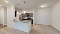 This single-story residence features two bedrooms and two bathrooms within a thoughtfully designed, open layout. The kitchen serves as a central highlight, showcasing dark espresso cabinetry, granite countertops, a large peninsula with pendant lighting, and a full suite of stainless steel appliances including a refrigerator, range, microwave, and dishwasher. Wood-look flooring runs throughout the kitchen, creating a clean, contemporary aesthetic that transitions naturally into the surrounding living areas.

The living space is carpeted and bathed in natural light from a sliding glass door fitted with vertical blinds, complemented by crown molding and a ceiling fan overhead. Both bedrooms are carpeted and feature neutral tones, with windows allowing in natural light. The primary bathroom includes a granite-topped double vanity with dark cabinetry, a large framed mirror, and a soaking tub, while the second bathroom mirrors the same design language with matching cabinetry, granite counters, and a tub-shower combination. A built-in shelving niche adds a practical architectural detail, and wood-look flooring carries through all wet areas, tying the overall design together cohesively.