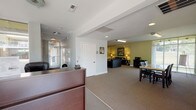 The Parkside Apartments leasing office is a well-organized, single-floor community facility designed to welcome and serve residents and prospective tenants alike. The space is anchored by a bright, glass-enclosed entrance lobby featuring floor-to-ceiling windows and double glass doors that flood the area with natural light and offer clear views of the surrounding streetscape. A polished terrazzo floor and a dedicated reception desk positioned near the entrance provide a professional first impression, making it easy for visitors to be greeted promptly upon arrival.

Adjacent to the reception area is a carpeted meeting zone furnished with a wooden table and dark chairs, ideal for leasing consultations or small group gatherings. The neutral gray and white tones of this area create a calm, professional atmosphere.

Beyond the front office, the space transitions into a generously sized resident lounge finished in warm sage green. This comfortable area is furnished with dark leather sofas, accent chairs, and side tables with lamps, creating an inviting retreat. The lounge is well-equipped with a wall-mounted flat-screen television, a water cooler, a full-size refrigerator, and a microwave — offering practical amenities for resident use. Artwork on the walls and thoughtful lighting add character and warmth throughout, making this leasing office both functional and welcoming.