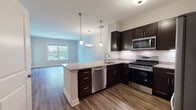 Located at 380 Mather St in Hamden, Connecticut, this well-appointed single-floor residence offers a thoughtfully designed open-concept layout that seamlessly connects the kitchen, dining, and living areas. The kitchen is a standout feature, showcasing rich dark cabinetry, granite countertops, and a full suite of stainless steel appliances including a gas range, built-in microwave, dishwasher, and refrigerator. A peninsula with pendant lighting above provides additional counter space and serves as a natural transition into the dining and living areas. Hardwood-style flooring runs consistently throughout the unit, lending a warm and cohesive aesthetic to each room. The living and dining area is generously sized, bathed in natural light from a large window with views of surrounding greenery, and accented by a stylish chandelier. The bedroom features the same durable flooring and neutral-toned walls, offering a clean, move-in-ready canvas. The bathroom is finished with a full tub and shower combination, chrome fixtures, and dark cabinetry that echoes the kitchen's design palette. Neutral wall tones throughout the space create a bright, airy atmosphere that complements the modern finishes.