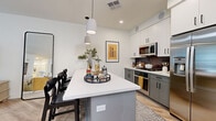 Located on Camelback Road in Phoenix, Arizona, this well-designed one-bedroom, one-bathroom residence offers a thoughtfully organized single-floor layout. The open-concept living area seamlessly connects the kitchen, dining, and living spaces, creating an efficient and inviting atmosphere.

The kitchen is a standout feature, showcasing a two-tone design with white upper cabinets and gray lower cabinets accented by a dark tile backsplash. A white quartz island with bar seating serves as both a functional workspace and casual dining area, illuminated by modern pendant lighting. Stainless steel appliances, including a French door refrigerator, microwave, and gas range, complete the space.

The dining area accommodates a full-sized wood table with woven chairs, complemented by recessed lighting and light wood-style flooring that extends throughout the unit. The living room offers a clean, minimal aesthetic with neutral walls and ample room for furnishings.

The bedroom is comfortably sized with a dedicated closet featuring built-in shelving and hanging storage. The bathroom includes a glass-enclosed walk-in shower with white subway tile and contemporary fixtures. Clean lines, neutral tones, and consistent finishes throughout contribute to a cohesive and modern living environment.