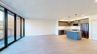 This contemporary 2-bedroom, 3-bathroom residence spans a single floor and features a thoughtfully designed open-concept layout that seamlessly connects the kitchen, dining, and living areas. Light hardwood flooring flows throughout, complementing the clean white walls and recessed lighting that maintain a bright, modern aesthetic.

The kitchen is a standout feature, boasting a distinctive blue center island with a white quartz countertop, dark gray cabinetry, stainless steel appliances including a gas range and refrigerator, a white tile backsplash, and stylish black cone pendant lights. Large floor-to-ceiling sliding glass doors in the living area invite abundant natural light and open directly to a private balcony offering urban and treetop views.

The primary bedroom features expansive floor-to-ceiling sliding glass doors with balcony access, filling the room with natural light and sweeping outdoor views. A spacious walk-in closet with wrap-around hanging rails provides generous storage. The secondary bedroom includes a built-in closet with sliding doors and warm hardwood flooring.

All three bathrooms are finished in a clean, modern style. The full bathrooms feature large-format gray tile surrounds, soaking tubs, floating gray vanities, and white quartz countertops. A hallway with built-in shelving connects the living spaces to the bedrooms, completing this well-appointed residence.