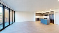 This contemporary 2-bedroom, 3-bathroom residence spans a single floor and features a thoughtfully designed open-concept layout that seamlessly connects the kitchen, dining, and living areas. Light hardwood flooring flows throughout, complementing the clean white walls and recessed lighting that maintain a bright, modern aesthetic.

The kitchen is a standout feature, boasting a distinctive blue center island with a white quartz countertop, dark gray cabinetry, stainless steel appliances including a gas range and refrigerator, a white tile backsplash, and stylish black cone pendant lights. Large floor-to-ceiling sliding glass doors in the living area invite abundant natural light and open directly to a private balcony offering urban and treetop views.

The primary bedroom features expansive floor-to-ceiling sliding glass doors with balcony access, filling the room with natural light and sweeping outdoor views. A spacious walk-in closet with wrap-around hanging rails provides generous storage. The secondary bedroom includes a built-in closet with sliding doors and warm hardwood flooring.

All three bathrooms are finished in a clean, modern style. The full bathrooms feature large-format gray tile surrounds, soaking tubs, floating gray vanities, and white quartz countertops. A hallway with built-in shelving connects the living spaces to the bedrooms, completing this well-appointed residence.